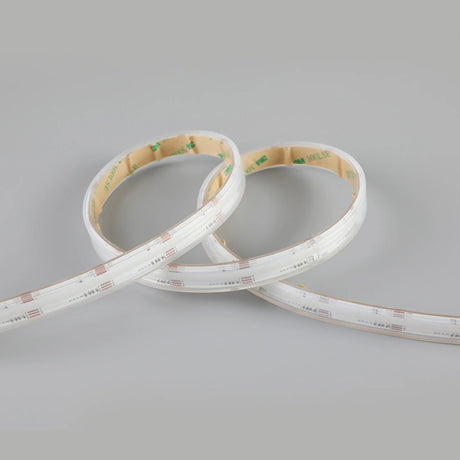 The EnoLED UniColor Series RGB+CCT COB IP67 High CRI LED Strip (24V) is shown coiled with a white casing and adhesive backing, set against a plain gray background.