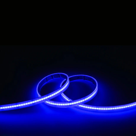 The EnoLED UniColor Series RGB+CCT COB IP67 High CRI LED Strip (24V) emits a striking blue glow in the dark, forming loose loops and illuminating the surface below with vivid, high-quality light.
