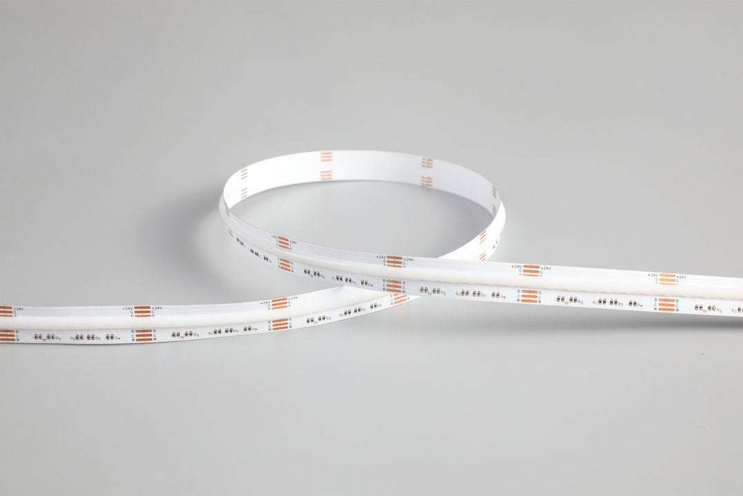 The RGB+CCT COB IP20 High CRI LED Strip (24V) ~ EnoLED UniColor Series, featuring a white base and visible orange and silver components, is coiled and displayed on a plain gray surface.