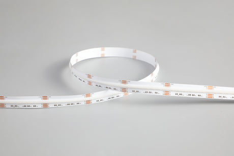 The RGB+CCT COB IP20 High CRI LED Strip (24V) ~ EnoLED UniColor Series, featuring a white base and visible orange and silver components, is coiled and displayed on a plain gray surface.