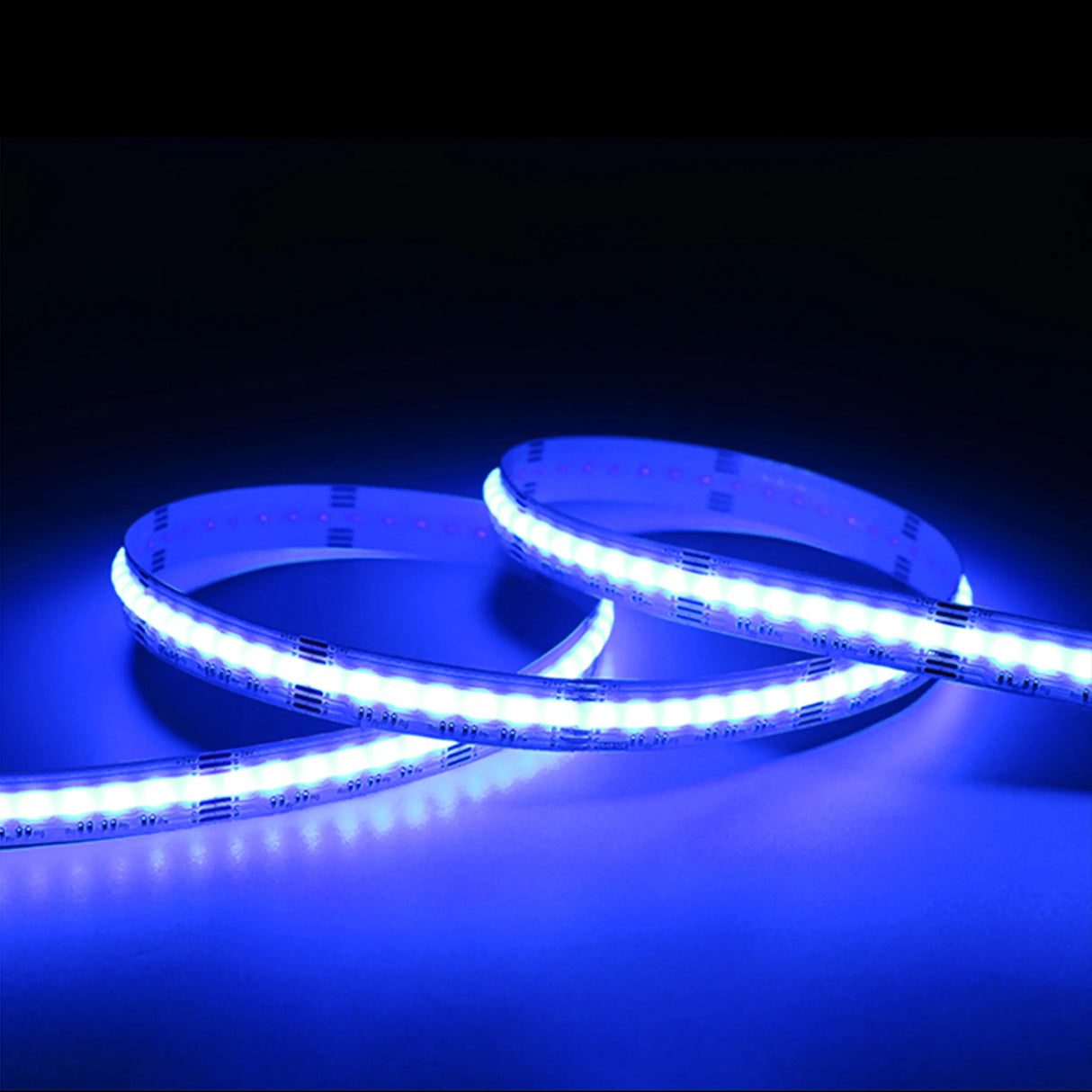 The RGB+CCT COB IP20 High CRI LED Strip (24V) ~ EnoLED UniColor Series emits a vivid blue glow, coiled in loops against a dark background and brightly illuminating the surrounding area.