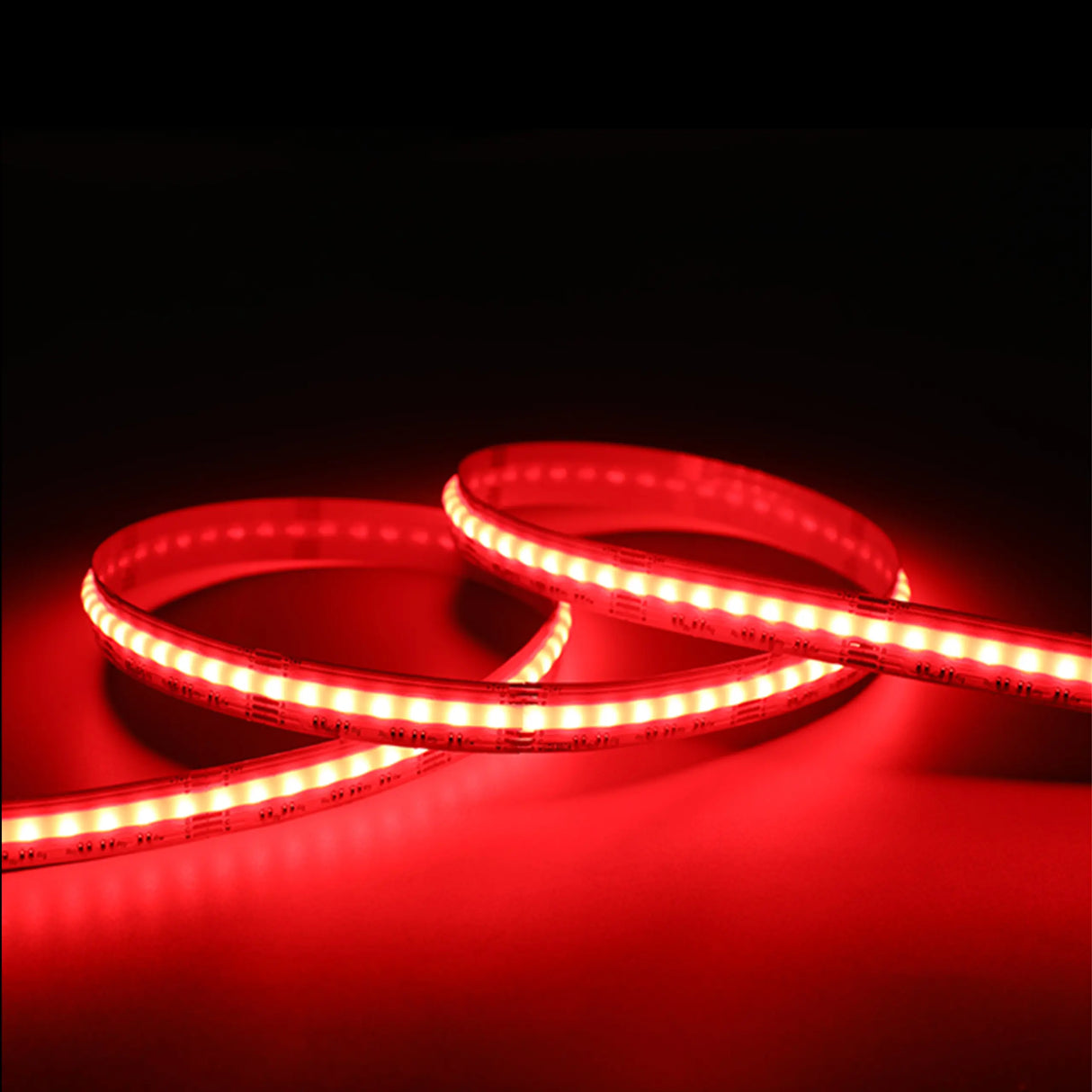 A close-up of the EnoLED UniColor Series RGB+CCT COB IP20 High CRI LED Strip (24V) glowing bright red, coiled loosely on a flat surface against a dark background.