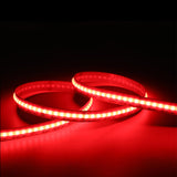 A close-up of the EnoLED UniColor Series RGB+CCT COB IP20 High CRI LED Strip (24V) glowing bright red, coiled loosely on a flat surface against a dark background.