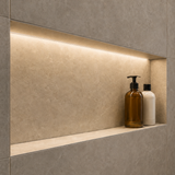 Two bottles, one amber with a pump and one white with a black cap, sit on a recessed shelf in a tiled wall, illuminated from above by the Tile Edge LED Strip Light Channel ~ Model Uni-Tile12 180Deg.