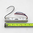 The Slimline Small Constant Voltage LED Driver (24V) from the ERP Power VLM Series is a compact, rectangular power supply with red, blue, black, and white wires pictured on a white surface beside a yellow tape measure showing its 16 cm length.