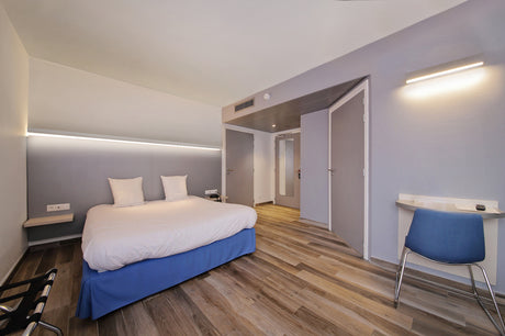 A modern hotel room with a double bed, wood floors, and minimalistic decor features sleek architectural lighting using the 1.3" Surface Mount Side-Lighting LED Channel (Model Vario30-03).