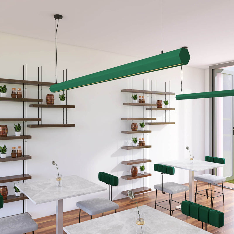 A modern dining or cafe interior with long green linear pendant lights hanging over white tables and chairs. The room has white walls, wood shelving with small plants and bottles, and a wood floor.