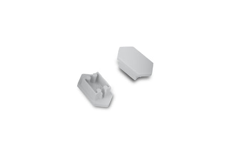 Two small white plastic C End Caps for Arc12 Duo Profile lighting fixture—each with angled sides—are shown on a plain white background; one end cap is facing up to display two pegs and a slot, while the other is facing down.