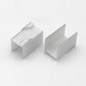 Two small, white, rectangular Visby Drop Ceiling T-Bar Clips with open U-shaped channels are shown on a white background at different angles to display their shape and structure—ideal for mounting to Visby profiles.