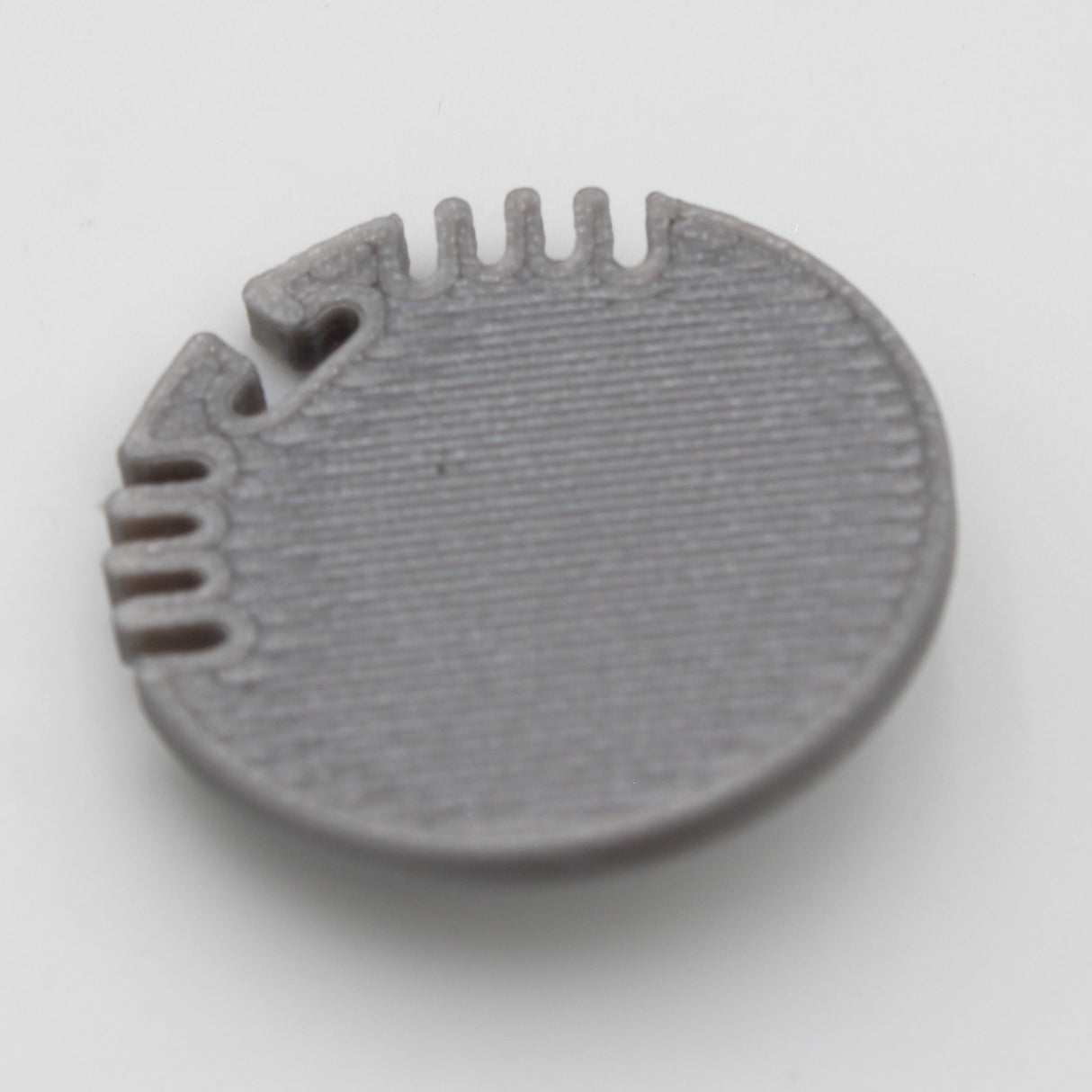 A gray plastic End Cap for Alu Round Profile, round and flat with a textured surface and evenly spaced edge notches and grooves—perfect for finishing your profile—shown on a plain white background.