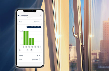 A smartphone shows the openSensor by Blebox app’s history bar chart for an open window, with a bright cityscape and sunlight streaming into the room.