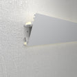 A close-up of the Up and Down Ceiling Wall Wash LED Profile ~ Model Badalona shows its textured white finish, internal structure, and soft illumination against a white textured wall, ideal for versatile lighting applications.