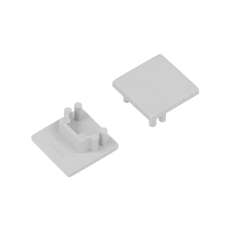 Two small, square, light gray plastic End Caps for Cozy12 Profile are shown. One cap features four pegs and a U-shaped ridge underneath for mounting; the other has a smooth top surface.