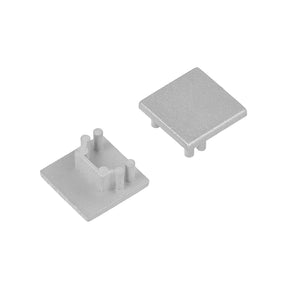 Two small, square gray End Caps for Cozy12 Profile are shown. One is upside down, revealing four round pegs and a central divider; the other is upright with a smooth surface, perfect for finishing Cozy12 profile lighting fixtures.