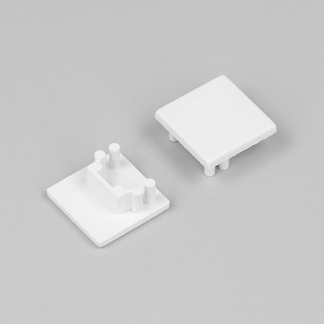 Two small, white, square plastic End Caps for Cozy12 Profile are shown on a plain gray background. Each has protruding pegs on one side, indicating they are designed to fit together as part of the Cozy12 lighting fixture.
