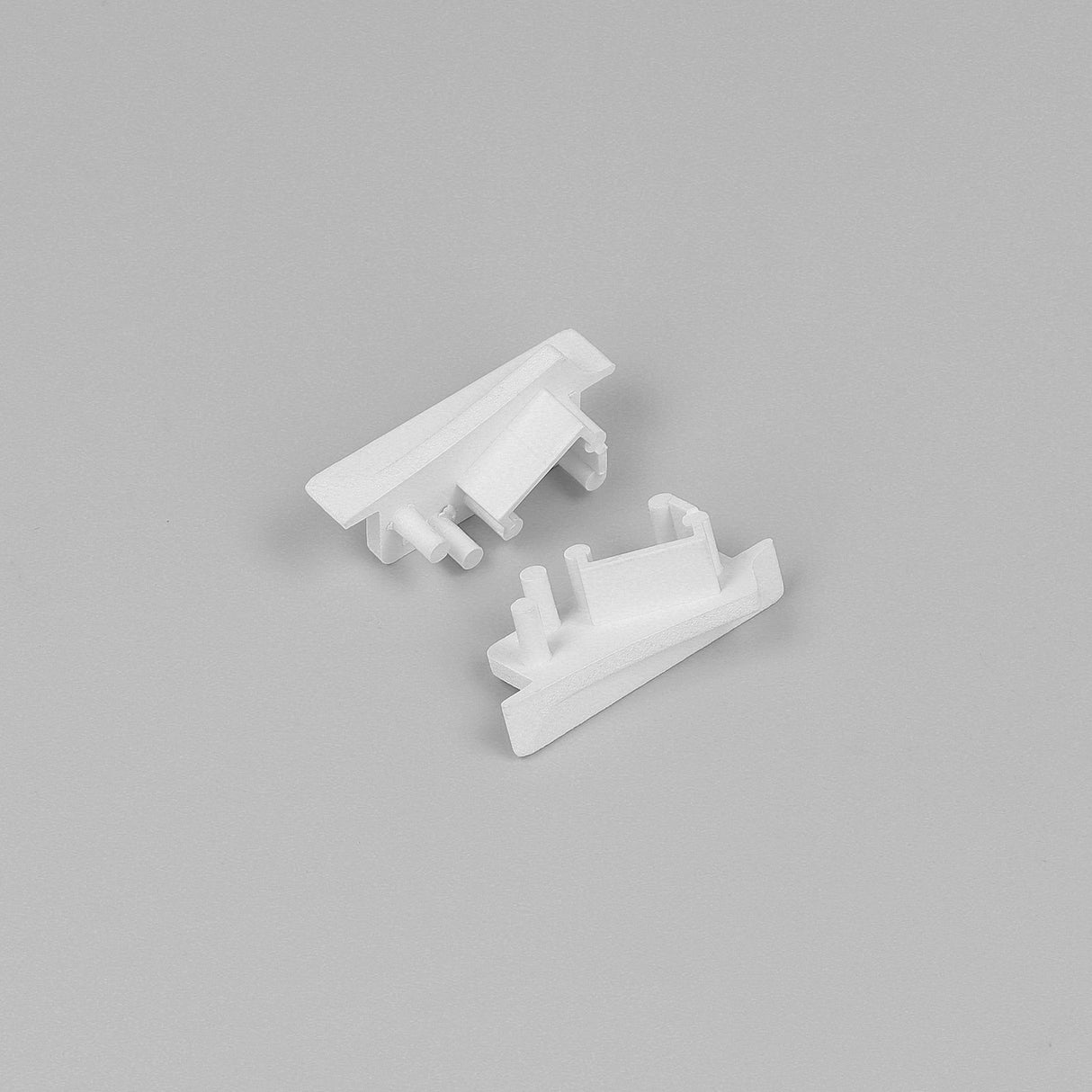 Two small, white End Caps for Diagonal10 Profile, featuring angular shapes and protruding pegs, are displayed on a plain light gray background.