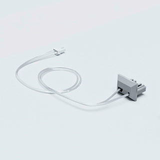 A transparent cable links a small, rectangular gray Cut & Connect End Cap for Roma Profile to a linear lighting system, both placed on a light gray surface.
