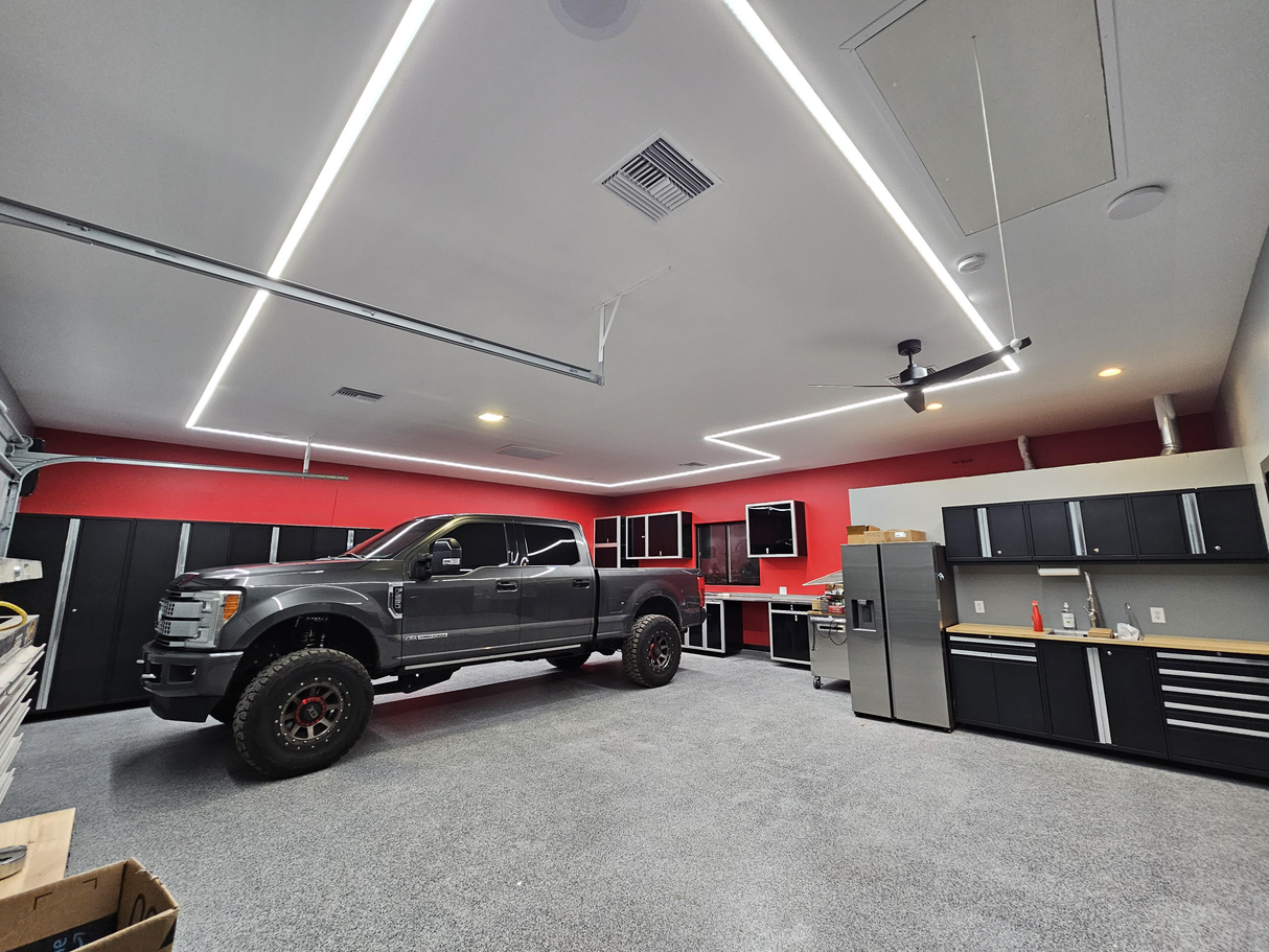 A modern garage with gray cabinets, a stainless steel fridge, a workbench, and a large black pickup truck. Red and white walls feature bold geometric ceiling patterns using SLW10 Surface Mount LED Strip Channel.