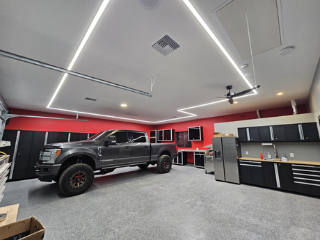 A modern garage with gray cabinets, a stainless steel fridge, a workbench, and a large black pickup truck. Red and white walls feature bold geometric ceiling patterns using SLW10 Surface Mount LED Strip Channel.