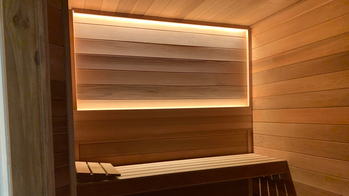 Sauna with warm LED strip lighting framing the back wall above the bench