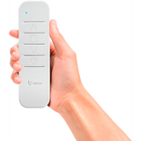 A hand holds the sRemote by Blebox, a white single channel battery-operated remote with up arrow, square, down arrow, and heart buttons, plus a blue indicator light and Blebox logo. Compatible with μWiFi-enabled BleBox devices.